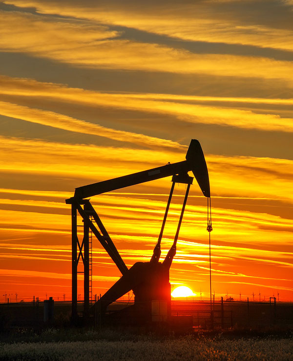 Silhouetted pump jack in the oil field at sunset