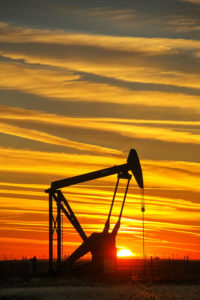 Silhouetted pump jack in the oil field at sunset